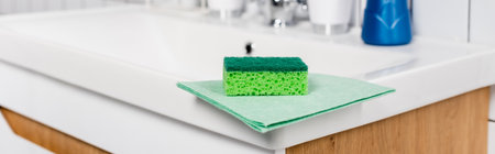 Green sponge and rag on sink in bathroom, banner