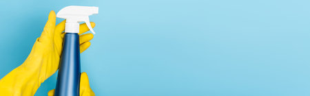 Cropped view of person in rubber gloves holding bottle of detergent on blue background, banner