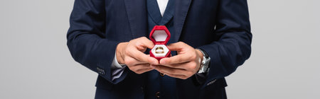 partial view of man in suit holding jewelry box with wedding ring isolated on gray, banner