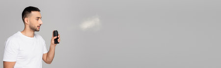brunette hispanic man in white t-shirt spraying deodorant isolated on gray with copy space, bannerの写真素材