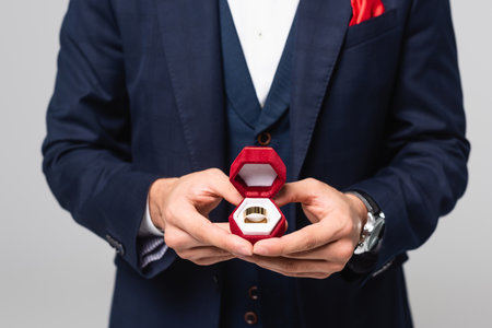 cropped view of elegant man holding jewelry box with wedding ring isolated on gray