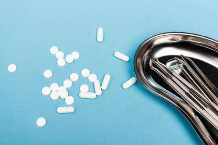 Pills near staleness dental tools on tray on blue background