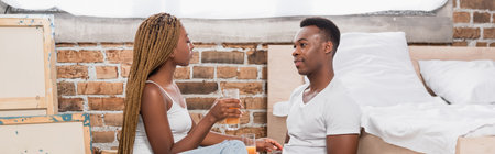 African american couple holding glasses of orange juice in bedroom, bannerの写真素材