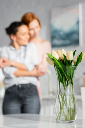 selective focus of tulips in vase near interracial lesbian couple hugging on blurred backgroundの写真素材
