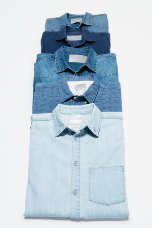 vertical row of blue denim shirts on white background, top view