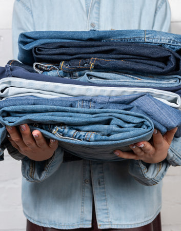 partial view of woman holding stacked denim clothesの写真素材