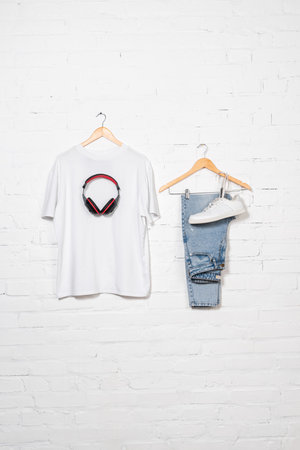 t-shirt, wireless headphones, blue jeans and sneaker on hangers near white brick wall