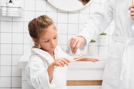 Mother squeezing toothpaste on brush near daughter in bathroomの写真素材
