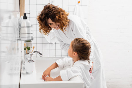Smiling woman hugging daughter near sink in modern bathroomの写真素材