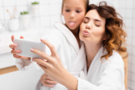 Smartphone in hands of mother and child posing for selfie on blurred background in bathroomの写真素材