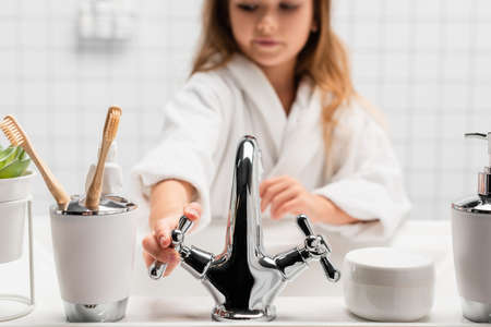Girl opening water near toiletries and sink on blurred backgroundの写真素材