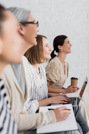 cheerful woman smiling near multicultural group of women during seminar on blurred foreground and backgroundの写真素材