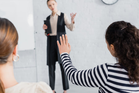 African american woman with raised hand near coworker and speaker of blurred background