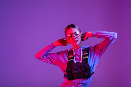 stylish woman in sunglasses posing isolated on purple with pink lighting and copy spaceの写真素材