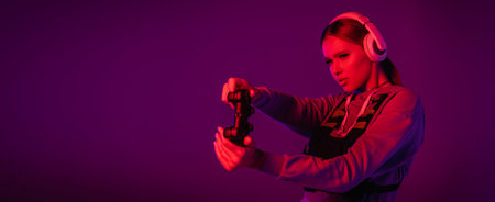 young woman in headphones playing video game on purple background, banner