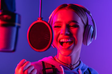 young singer in wireless headphones recording song while singing in microphone on blurred foregroundの写真素材