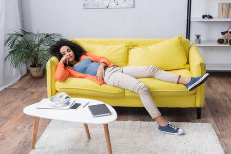bored african american woman chilling on yellow couchの写真素材