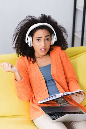 african american woman holding notebook and listening podcast in headphones