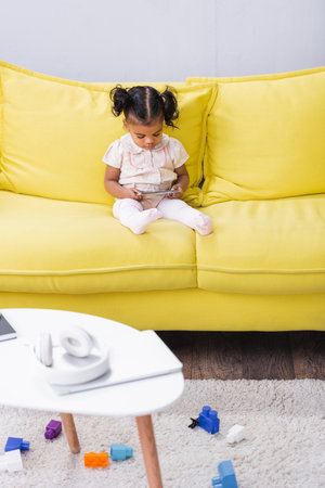 toddler african american girl using smartphone while sitting on sofaの写真素材
