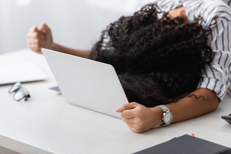 african american woman covering face while lying on laptop at homeの写真素材