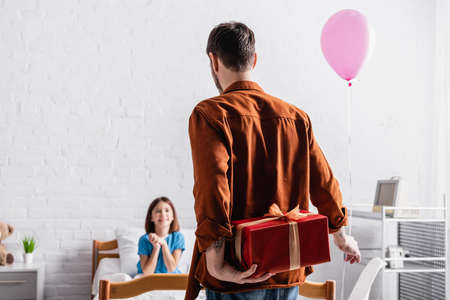 back view of man holding festive balloon and gift box near happy daughter on blurred backgroundの写真素材