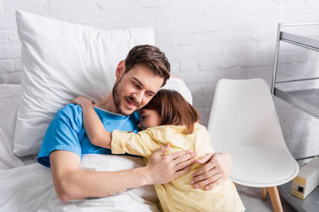 smiling man embracing daughter while lying in bed in hospitalの写真素材