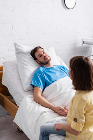 girl holding hand of diseased father lying in hospital bed
