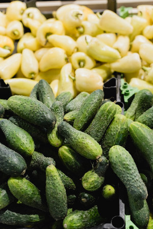 Fresh cucumbers near peppers on blurred background in supermarketの写真素材