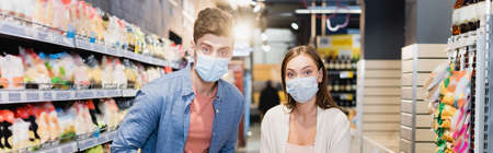 Young couple in medical masks looking at camera in supermarket, bannerの写真素材