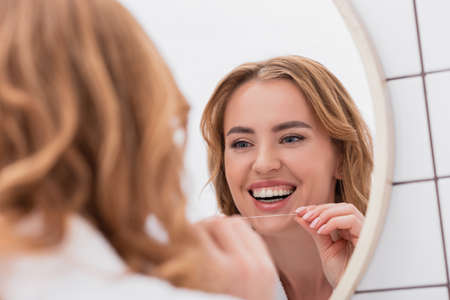 reflection of cheerful woman looking at mirror and holding dental floss
