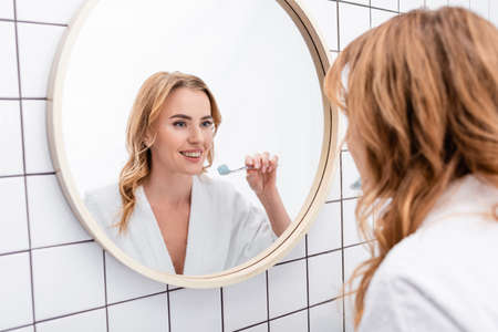 happy woman holding toothbrush with toothpaste near mirrorの写真素材