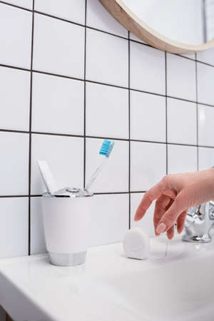 cropped view of woman reaching container with dental floss in bathroom