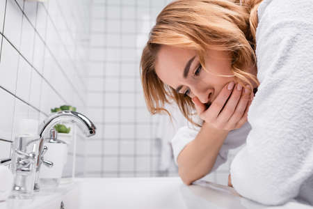 pregnant woman covering mouth while feeling nausea near sink in bathroomの写真素材