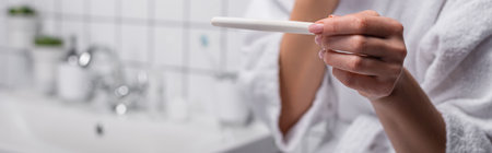partial view of woman holding pregnancy test in bathroom