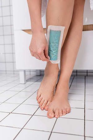 cropped view of woman removing wax stripe om leg in bathroomの写真素材