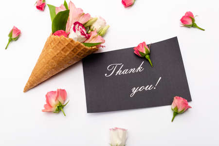top view of pink flowers in waffle cone near card with thank you lettering on whiteの写真素材