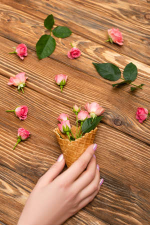 cropped view of woman holding waffle cone with pink tea roses on wooden surfaceの写真素材