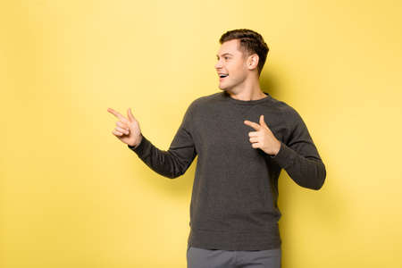 Smiling man pointing with fingers on yellow background