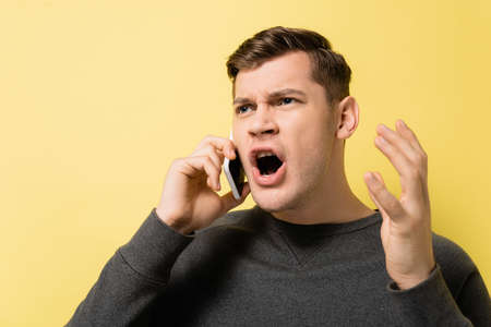 Embarrassed man talking on smartphone on yellow background