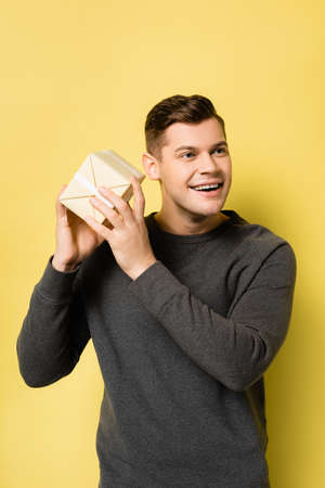 Cheerful man in gray pullover holding present on yellow backgroundの写真素材