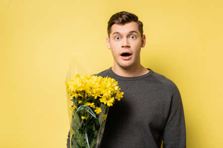 Amazed man with bouquet looking at camera on yellow backgroundの写真素材