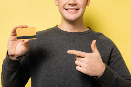 Cropped view of man pointing with finger at credit card on yellow backgroundの写真素材