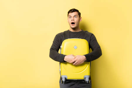Excited man hugging suitcase on yellow backgroundの写真素材