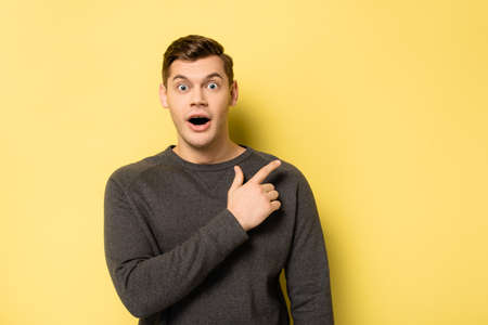 Excited man looking at camera and pointing with finger on yellow backgroundの写真素材