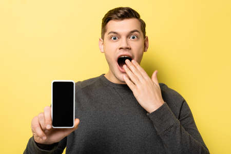 Astonished man showing smartphone with blank screen on yellow backgroundの写真素材