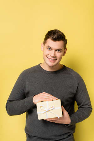 Happy man with present looking at camera on yellow background