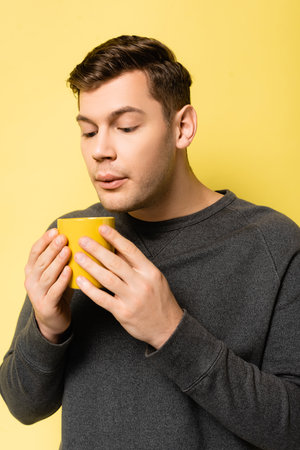 Young man blowing at mug on yellow backgroundの写真素材