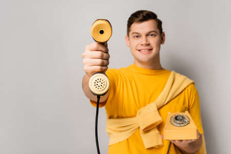 Yellow telephone handset in hand of smiling man blurred on gray backgroundの写真素材
