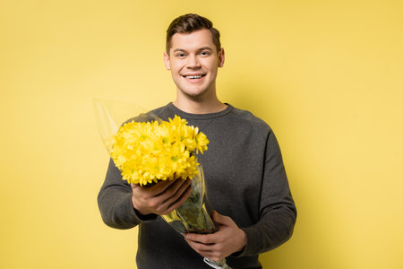 Cheerful man holding flowers on yellow backgroundの写真素材