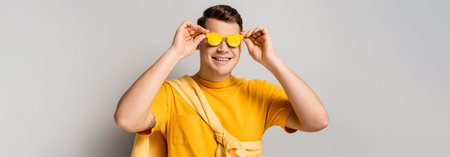 Happy man wearing yellow sunglasses on gray background, banner